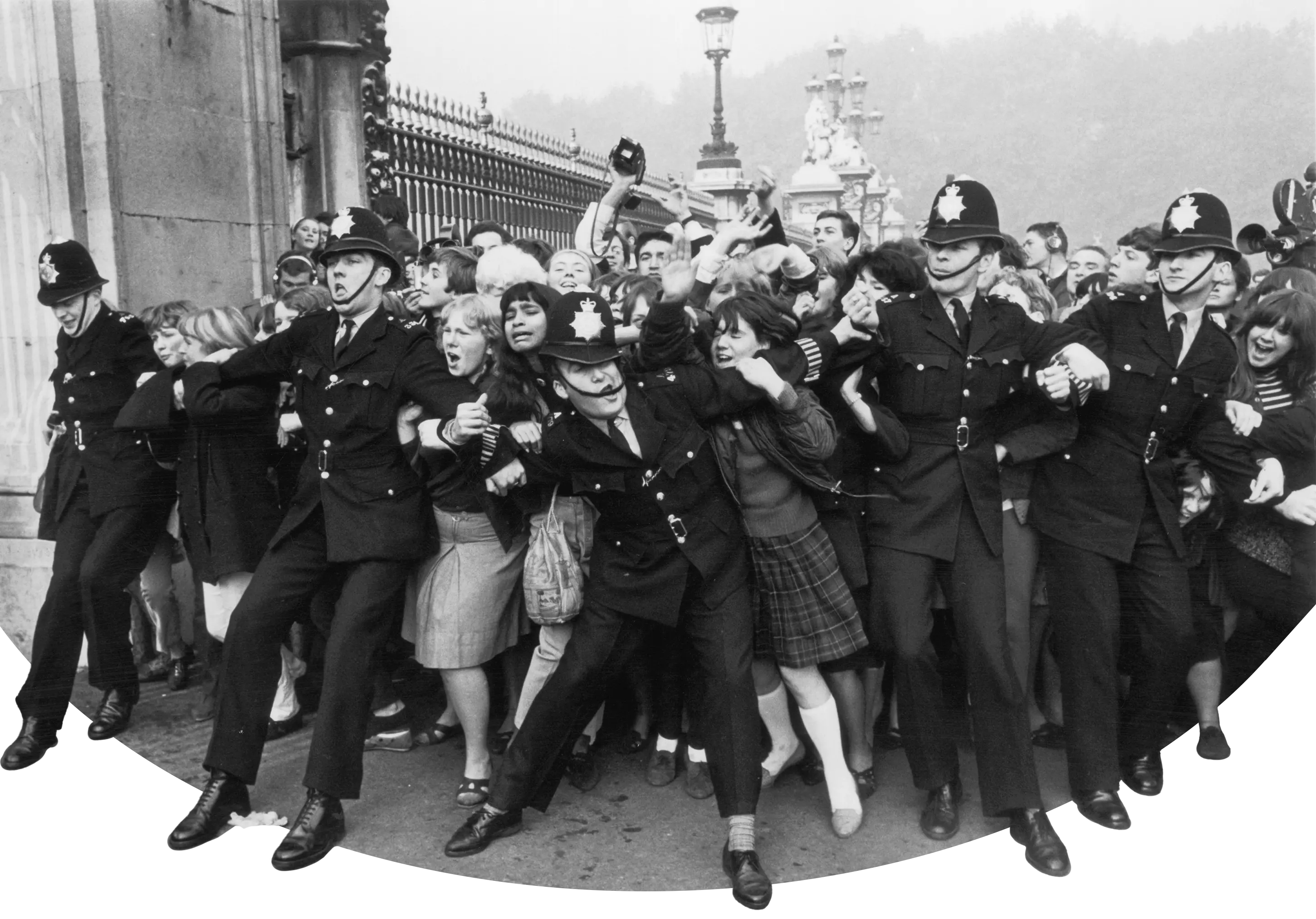 A line of police officers link arms to hold back a crowd of screaming fans at ornate iron gates